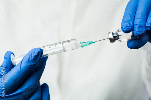 Nurse of NHS medical lab technician inserting syringe needle into glass vial bottle photo