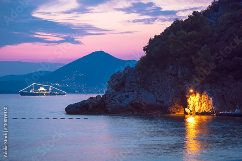 Stunning Montenegro Sunsets From Waterfront Restaurants Hotel Balconies And Seaside Cliffs. The photo is taken in the city of Sveti Stefan at sunset. In the distance we see a cruise ship.
