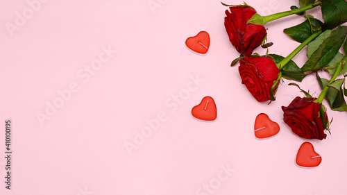 Bouquet of red roses and candles on a pink background, top view.