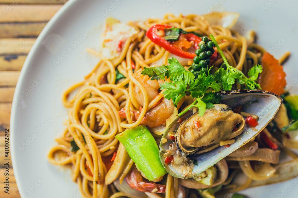 spicy spaghetti with shrimp, and mussel, on top with pepper on black plate. 
seafood pasta on dish, corn and herb leaf on wooden table
