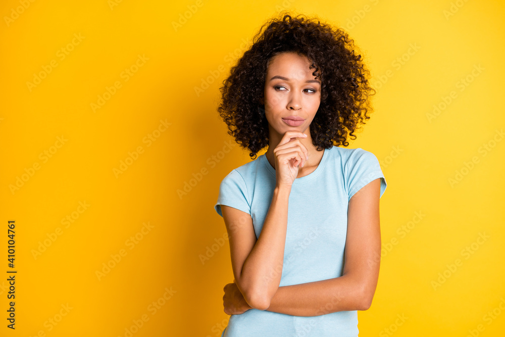 Photo of pretty serious dark skin wavy lady wear blue t-shirt arm chin looking empty space isolated yellow color background Photo of pretty serious dark skin wavy lady wear blue t-shirt arm chin looking empty space isolated yellow color background