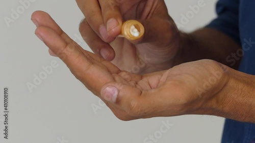 Close shot of male hand holding a tube medicine container and dropping small white round pills dosage on the other hand's palm