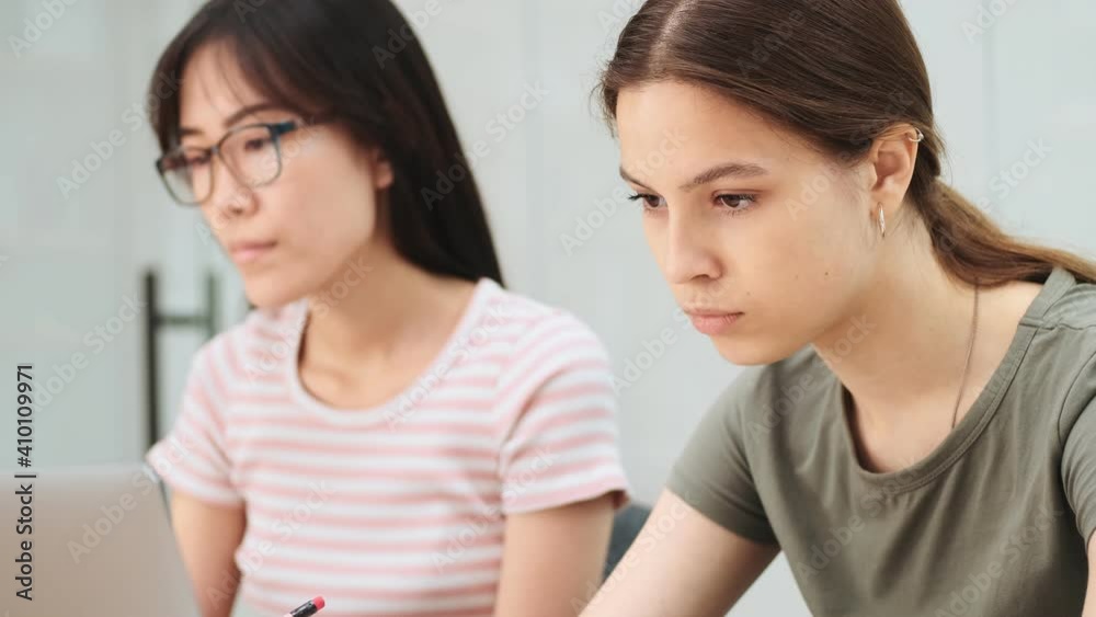 Close-up view of a two serious multinational women are working using laptops sitting in the office Close-up view of a two serious multinational women are working using laptops sitting in the office