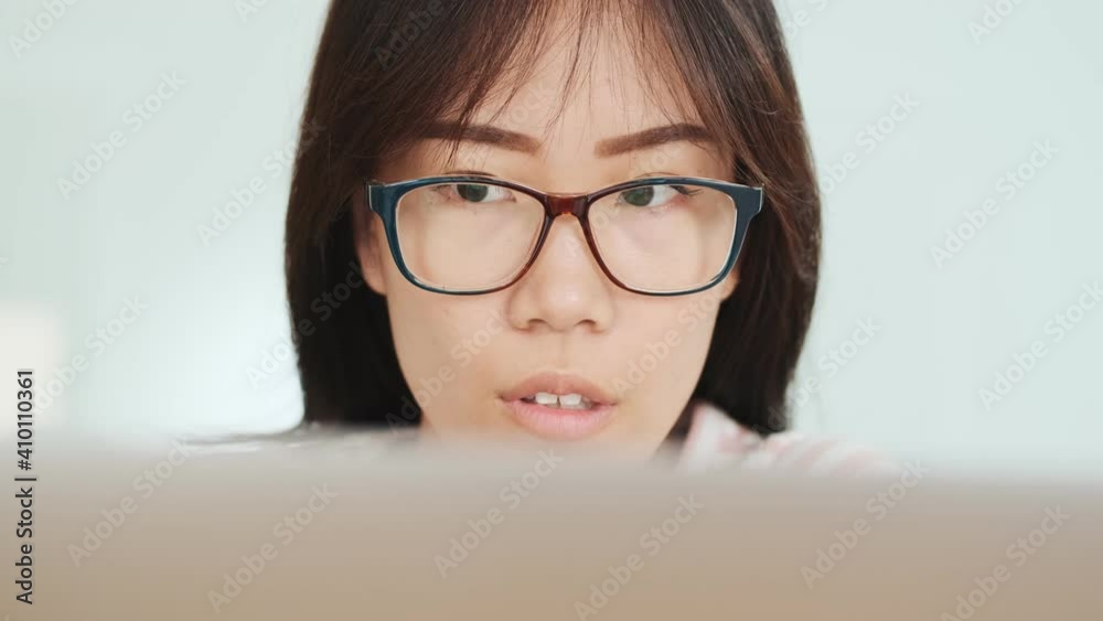 A close-up view of a concentrated asian woman is sitting at the table while working with laptop computer in the office A close-up view of a concentrated asian woman is sitting at the table while working with laptop computer in the office
