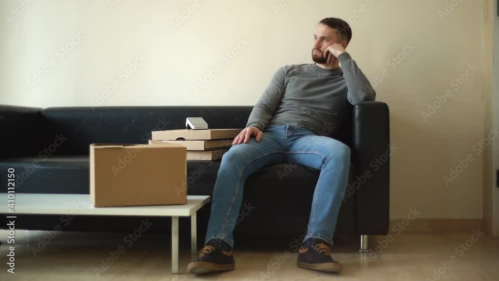 Handsome delivery man in casual clothes waiting for client while sitting on sofa in spacious lobby. Courier with boxes with hot pizza and parcel tapping his fingers nervously as he waits for customer. Handsome delivery man in casual clothes waiting for client while sitting on sofa in spacious lobby. Courier with boxes with hot pizza and parcel tapping his fingers nervously as he waits for customer.