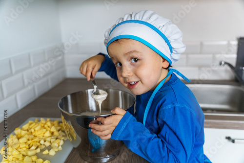 Adorable little boy helping and baking apple pie in home''s kitchen, indoor. Child  wearing apron and toque kneading and mixing dough photo