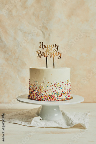 Vertical shot of a cake with a ''happy birthday'' cake topper and sprinkles on a tray on the table