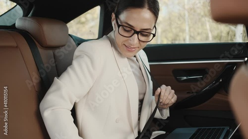 A beautiful young businesswoman wearing glasses is putting on safety belt using laptop computer sitting in the car  photo
