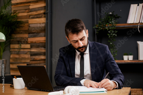 Young businessman using laptop in his office. Businessman taking a notes while working on laptop.