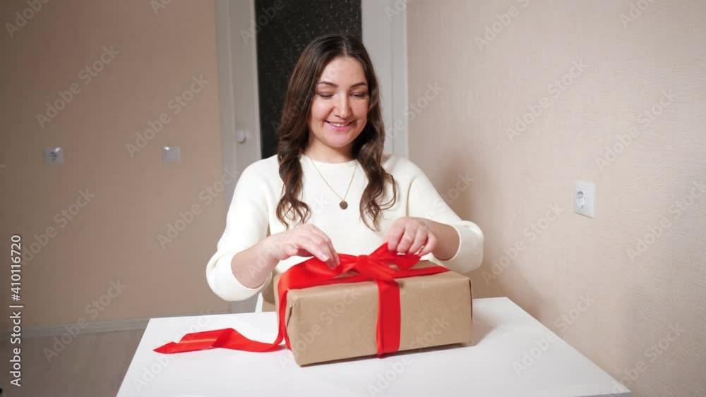 Beautiful brunette woman unpacks a gift sitting at the table. Beautiful brunette woman unpacks a gift sitting at the table.