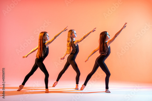 group of three girls in black tight-fitting suits dancing on red background with their long hair down.
