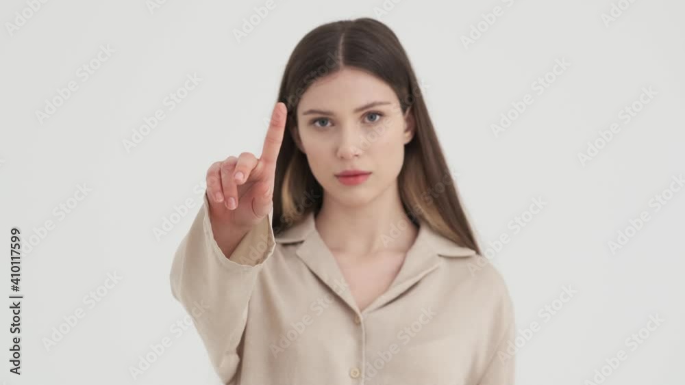 A confident young woman is shaking her finger doing stop gesture standing isolated over white background in stud A confident young woman is shaking her finger doing stop gesture standing isolated over white background in stud