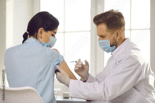 Man doctor in protective face mask reaching with syringe for woman patient arm for making vaccination against 19-ncov infection. Vaccinating against COVID-19 infection concept