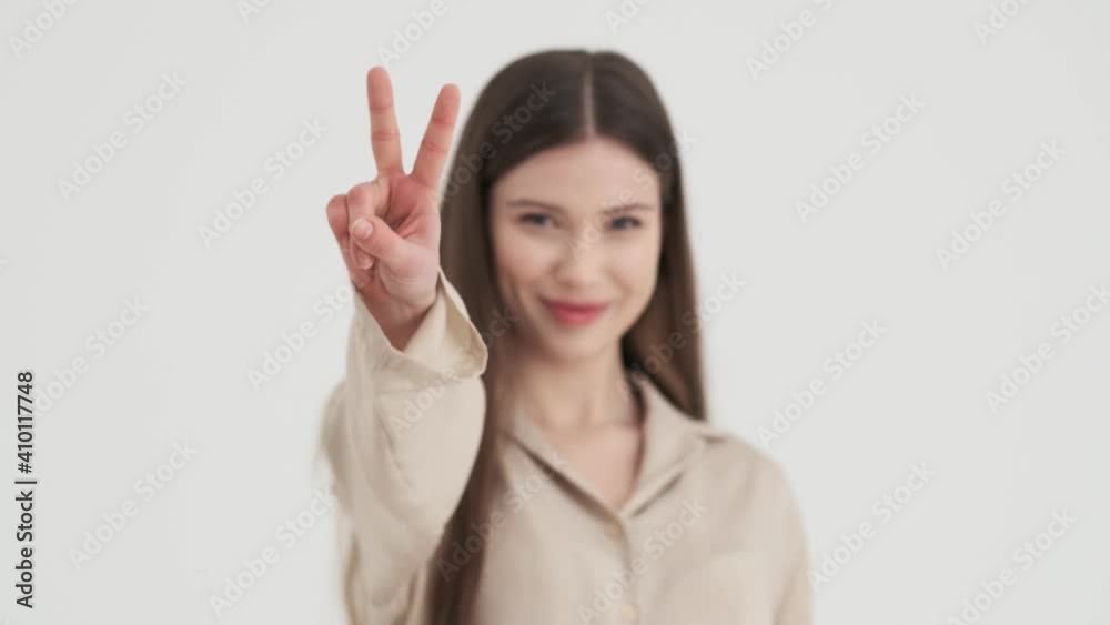A pleased young woman is showing peace gesture standing isolated over white background in studio A pleased young woman is showing peace gesture standing isolated over white background in studio