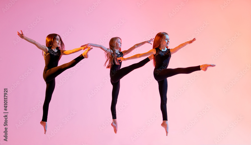 group of three ballet girls in black tight-fitting suits jumping on red background with their long hair down.