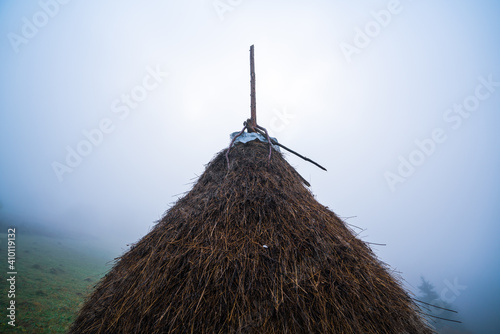 A large haystack stands on a green field among the dense gray fog photo