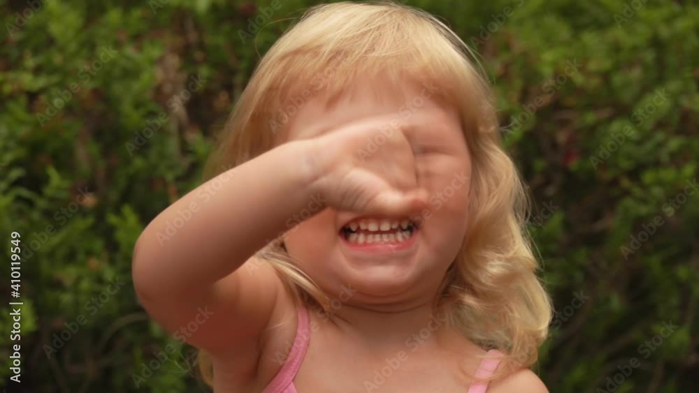Beautiful little blond girl is smiling and waving her hand to the camera in the sunny park outdoors Beautiful little blond girl is smiling and waving her hand to the camera in the sunny park outdoors