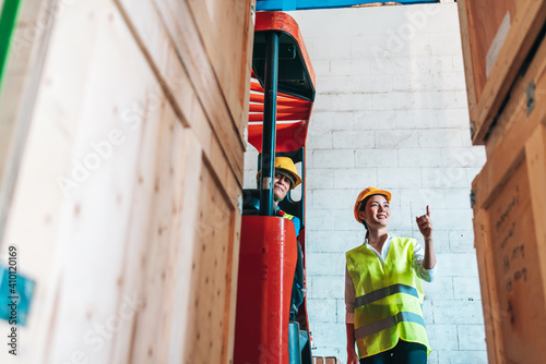 Portrait of asian woman. warehouse Smiling worker standing check box in large warehouse with goods. in background driver at Warehouse forklift loader works with goods.