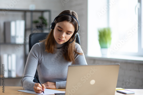 Beautiful young girl studying online using laptop web camera, writing lecture in notebook.Online education, remote working, home education.Online meeting,video call, video conference, courses online.