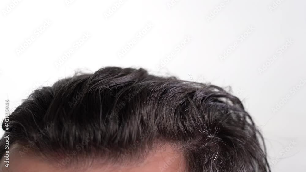 young man runs his hand through messy and shaggy hair on a white background. close-up young man runs his hand through messy and shaggy hair on a white background. close-up