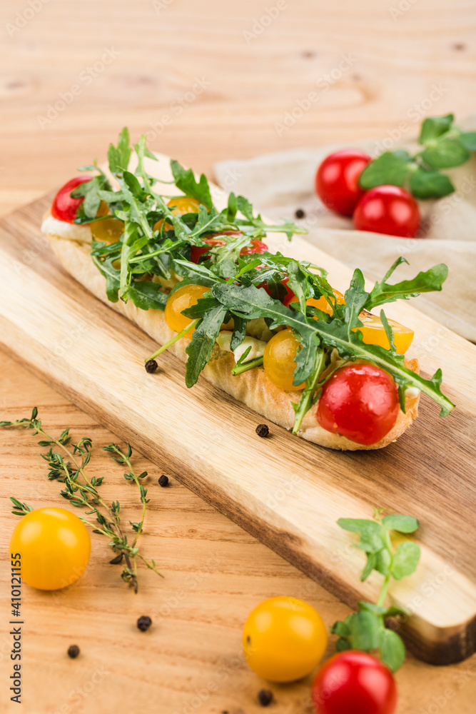 Bruschetta with mozzarella, cherry tomatoes and arugula with olive oil on a board on a light wooden background. Bruschetta with mozzarella, cherry tomatoes and arugula with olive oil on a board on a light wooden background.