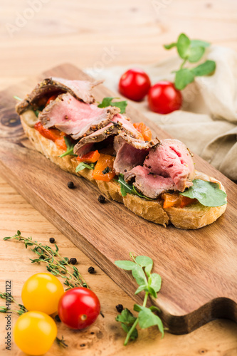Bruschetta with roast beef, fresh herbs and paprika on a board on a light wooden background.