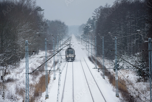Dwutorowy szlak kolejowy zimą z przejeżdżającą lokomotywą elektryczną.