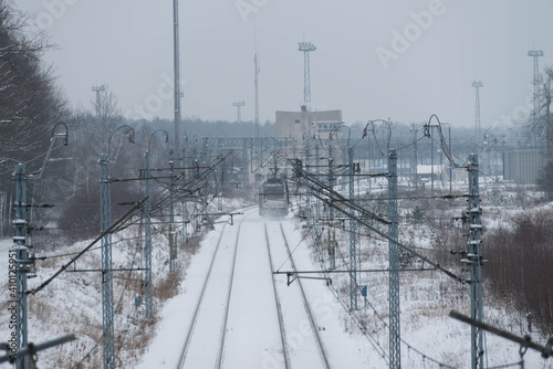 Dwutorowy szlak kolejowy zimą z przejeżdżającą lokomotywą elektryczną.