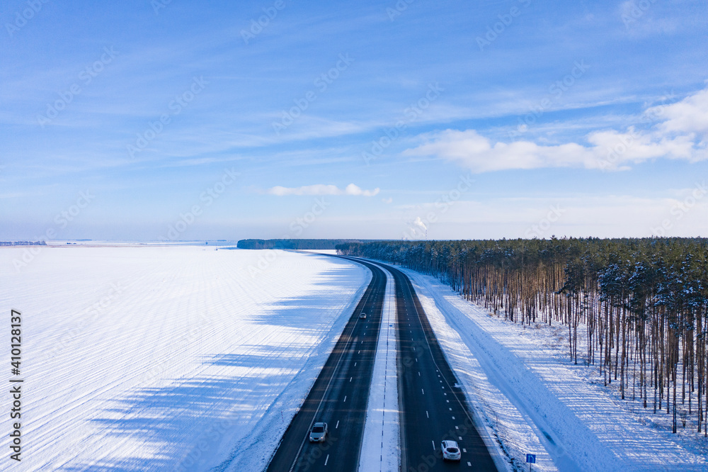 Asphalt road, track in winter. Winter Autobahn through the forest and field. Sunshine, frosty morning. Traveling by car in winter. View from above. 
