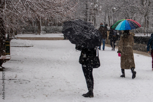 a woman with a black jacket holding a black umbrella on a park in a winter cold snowfall with a lot of snow