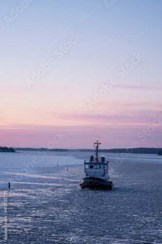 Beautiful sunset over the frozen water. Icebreaker ship breaking through the ice, proving safe waterways for other boats, ships and vessels during winter season. Photo taken in Sweden. © Susie Hedberg