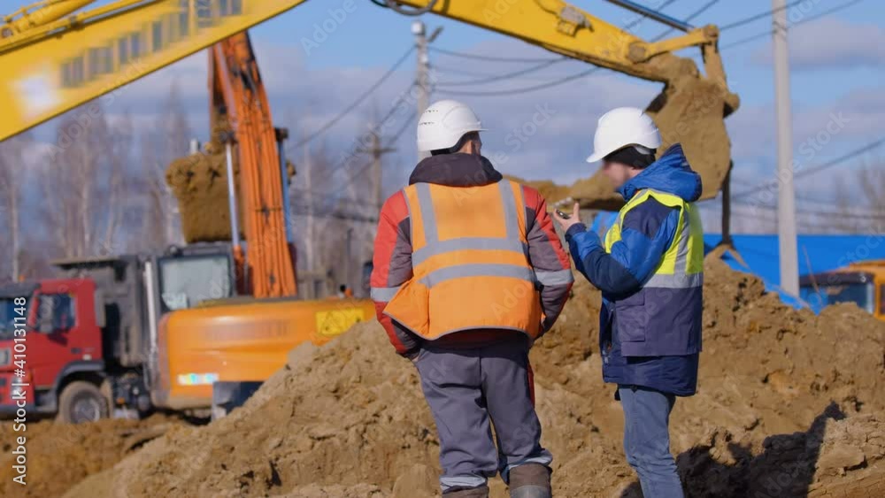 Earthwork at a construction site in winter,  excavators digs a place for a foundation, in the foreground, representatives of the contractor control the work of construction equipment 