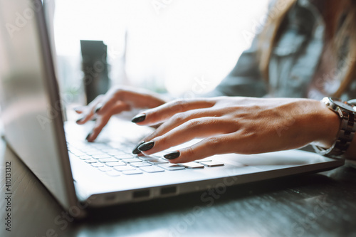 Close up of unrecognizable woman's hands with dark nailpolish using grey laptop computer on desk