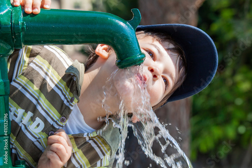 Kind trinkt Wasser aus Pumpbrunnen