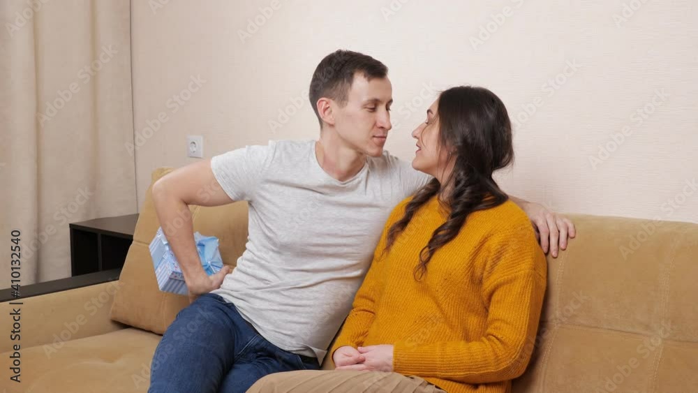 man giving a gift to a woman sitting on the couch. man giving a gift to a woman sitting on the couch.