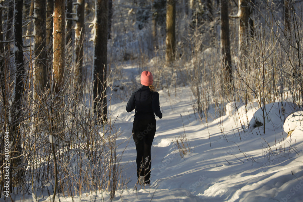 A young woman runs in the winter forest. Active lifestyle.