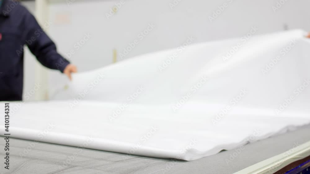 Employees put white spunbond cloth on cutting table in shop Employees put white spunbond cloth on cutting table in shop