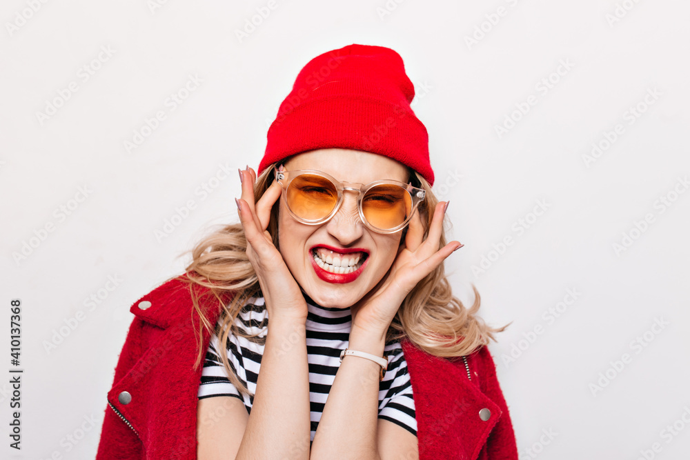 Woman in red hat and jacket has headache. Evil girl in sunglasses bares her teeth Woman in red hat and jacket has headache. Evil girl in sunglasses bares her teeth