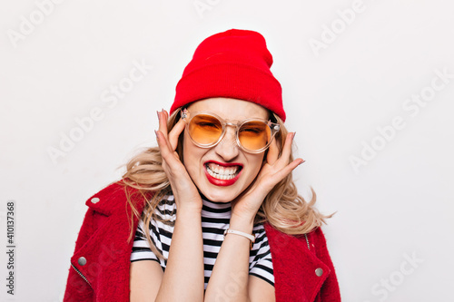 Woman in red hat and jacket has headache. Evil girl in sunglasses bares her teeth