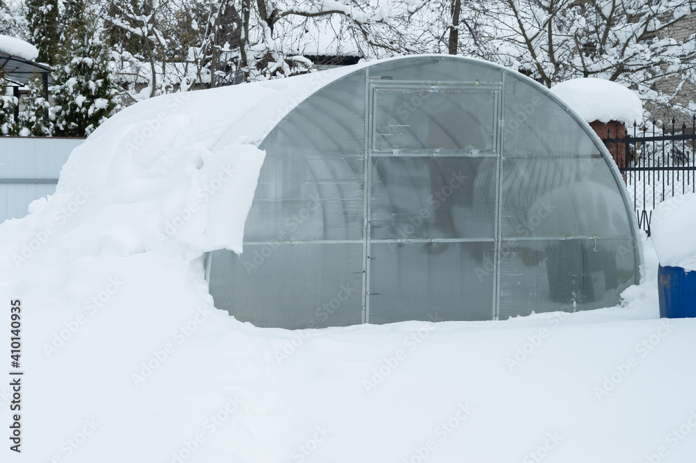 Greenhouse under the snow at winter. Modern acrylic polycarbonate glasshouse with aluminium arch frame. Snow removal concept Greenhouse under the snow at winter. Modern acrylic polycarbonate glasshouse with aluminium arch frame. Snow removal concept