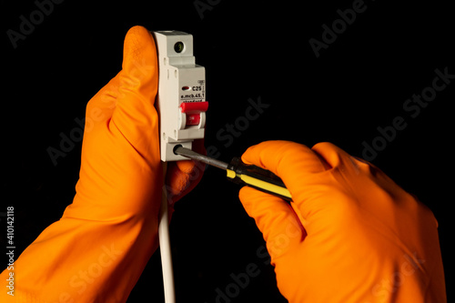 Electrician hands with gloves connect cable to Miniature Circuit Breaker with screwdriver photo