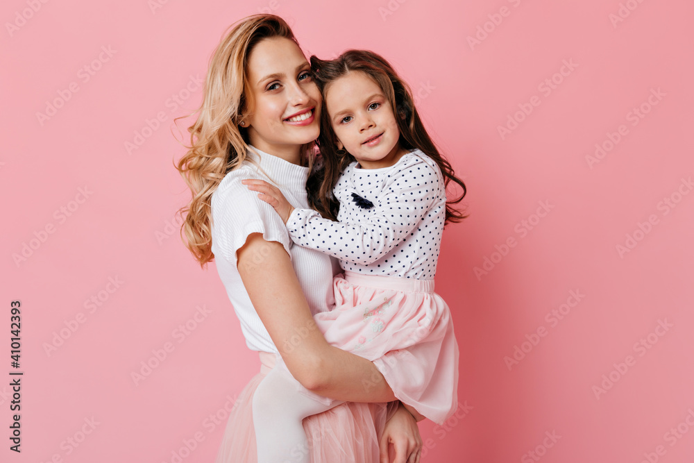 Close-up portrait of beautiful young mother and little daughter with smile posing on pink background Close-up portrait of beautiful young mother and little daughter with smile posing on pink background