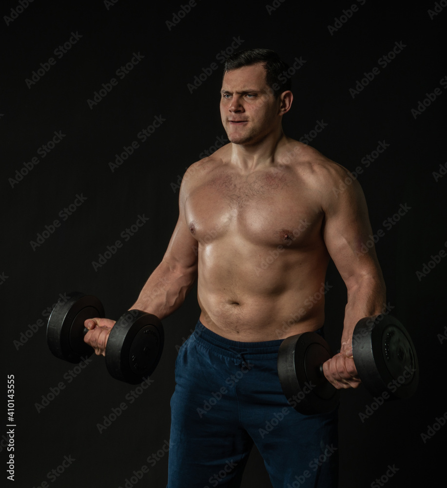 Man strains muscles with dumbbells pumps bicep bare torso Young male business portrait of a guy in the background. Beautiful content, success smile background black bodybuilder