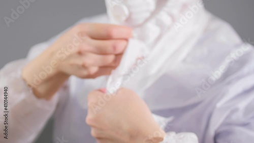 Medical worker in respirator ties hood bands on light grey photo