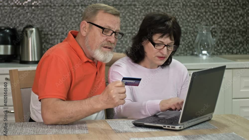 Friendly married couple using laptop at home for online shopping. Shopping during the coronavirus pandemic. Friendly married couple using laptop at home for online shopping. Shopping during the coronavirus pandemic.