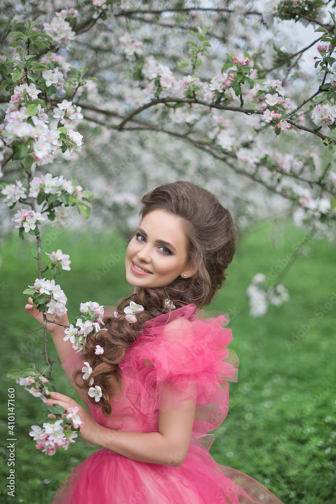 A beautiful young girl with long hair in a light pink ball gown walks through a blooming apple orchard A beautiful young girl with long hair in a light pink ball gown walks through a blooming apple orchard