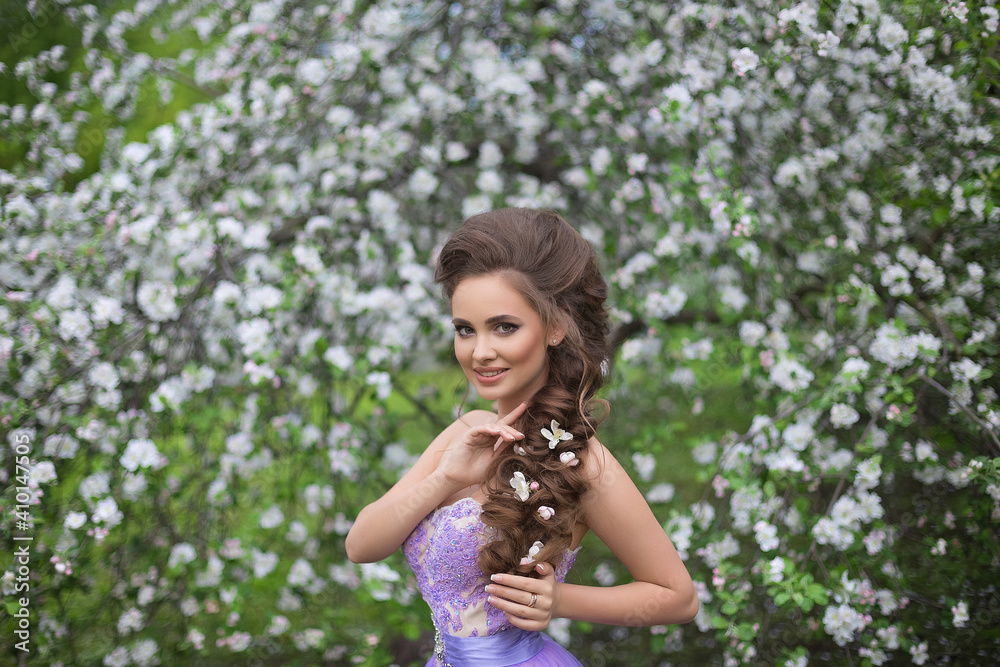 Portrait of a beautiful young girl with long hair in lilac dress on the background of a blooming apple orchard Portrait of a beautiful young girl with long hair in lilac dress on the background of a blooming apple orchard