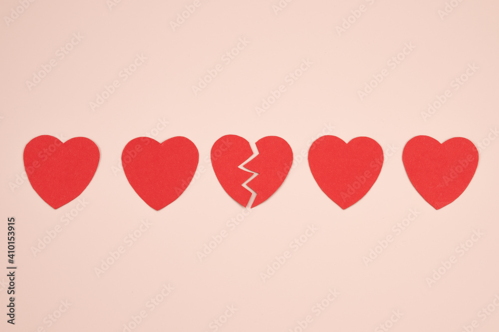 Red paper hearts on pink pastel background. A row of heart with one broken heart. Broken heart love relationship concept
