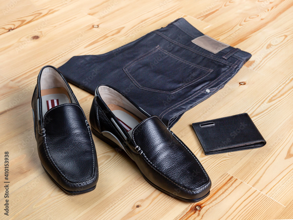 A pair of men's maccassin-style shoes next to jeans and a wallet against a light wooden surface A pair of men's maccassin-style shoes next to jeans and a wallet against a light wooden surface