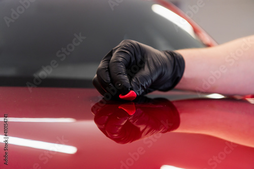 The master removes small dirt pieces from the car bonnet surface with special clay before polishing. Professional car washing and detailing process.
